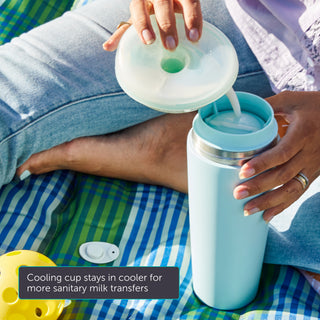 Person pouring breast milk into a seaglass Elvie breast milk cooler with a lid on a checkered blanket.
