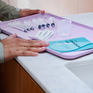 Tray with Elvie colostrum kit laid out including syringes, guide and a cup on a counter