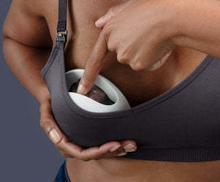 Person holding a black bra with a white Elvie Curve demonstrating one press expression.