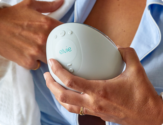 Person holding a white Elvie breast pump inserting into bra