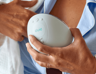 Person holding a white Elvie electric breast pump going to insert in-bra