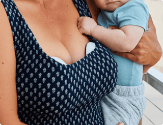 Woman holding a baby with an Elvie breast pump in bra