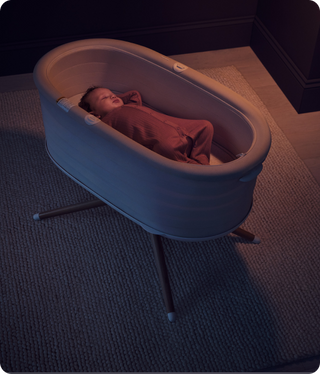 Baby sleeping in a an Elvie bassinet on a textured carpet