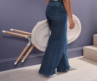 Person wearing blue jeans standing in a room with Elvie Rise folded flat and purple wall.