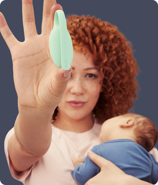 Woman holding a baby and showing a Elvie trainer against a dark background