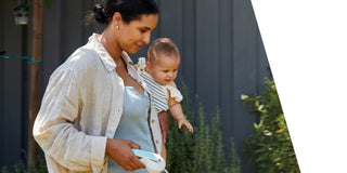 Woman holding a baby outdoors whilst using Elvie Wave manual breast pump.