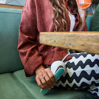 Person sitting on a green couch holding the Elvie Wave handle and pumping wearing a red sweater and patterned pants.