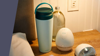 Elvie breast milk cooler in teal on bedside table next to Elvie breast pump