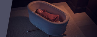 Baby asleep in Elvie Rise smart bassinet on cream carpet in dark room