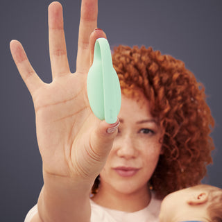 Woman holding a green Elvie trainer between her fingers against a dark background